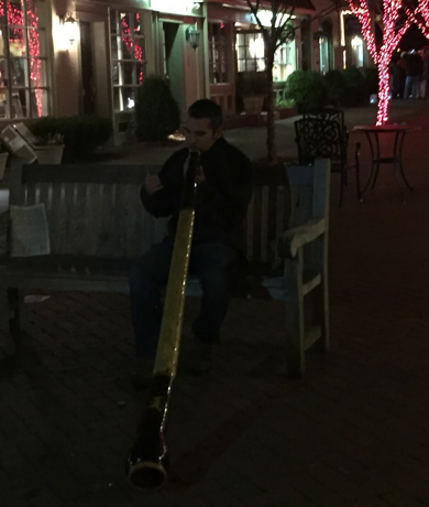One man sat on a bench playing the Australian wind instrument the didgeridoo.