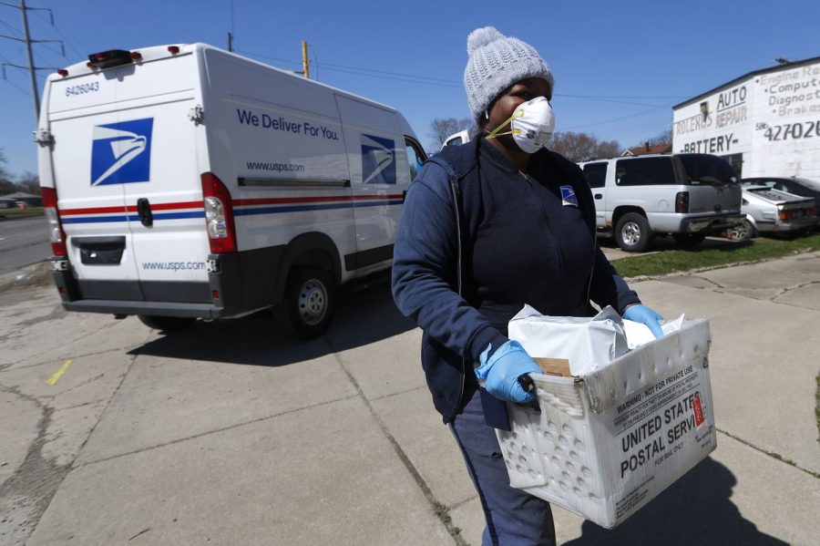 USPS worker carries a box of mail while wearing a mask