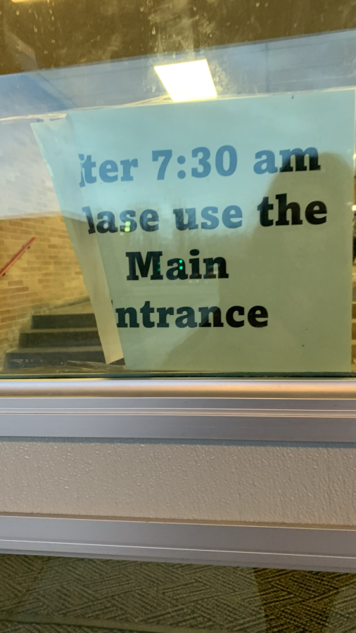 A sign posted outside of the school directing late students to use the Main Entrance.