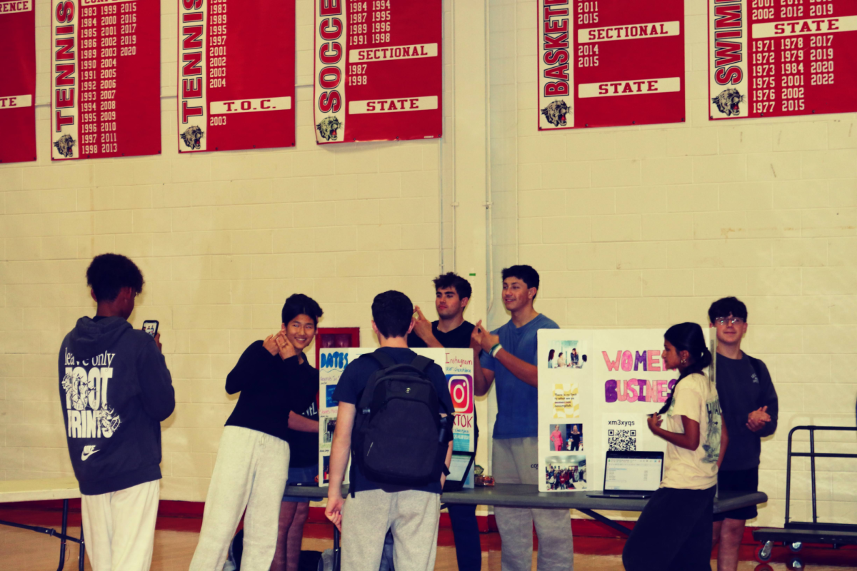 Students pose in front of a club's trifold. 